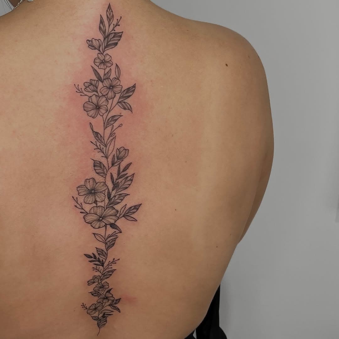 Fine-line black-and-grey wildflower vine running down the spine by AinsleyXTattoos