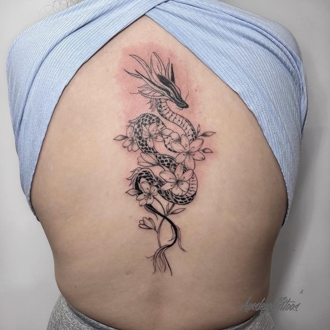 Fine-line dragon entwined with frangipani blossoms running down the spine by AinsleyXTattoos