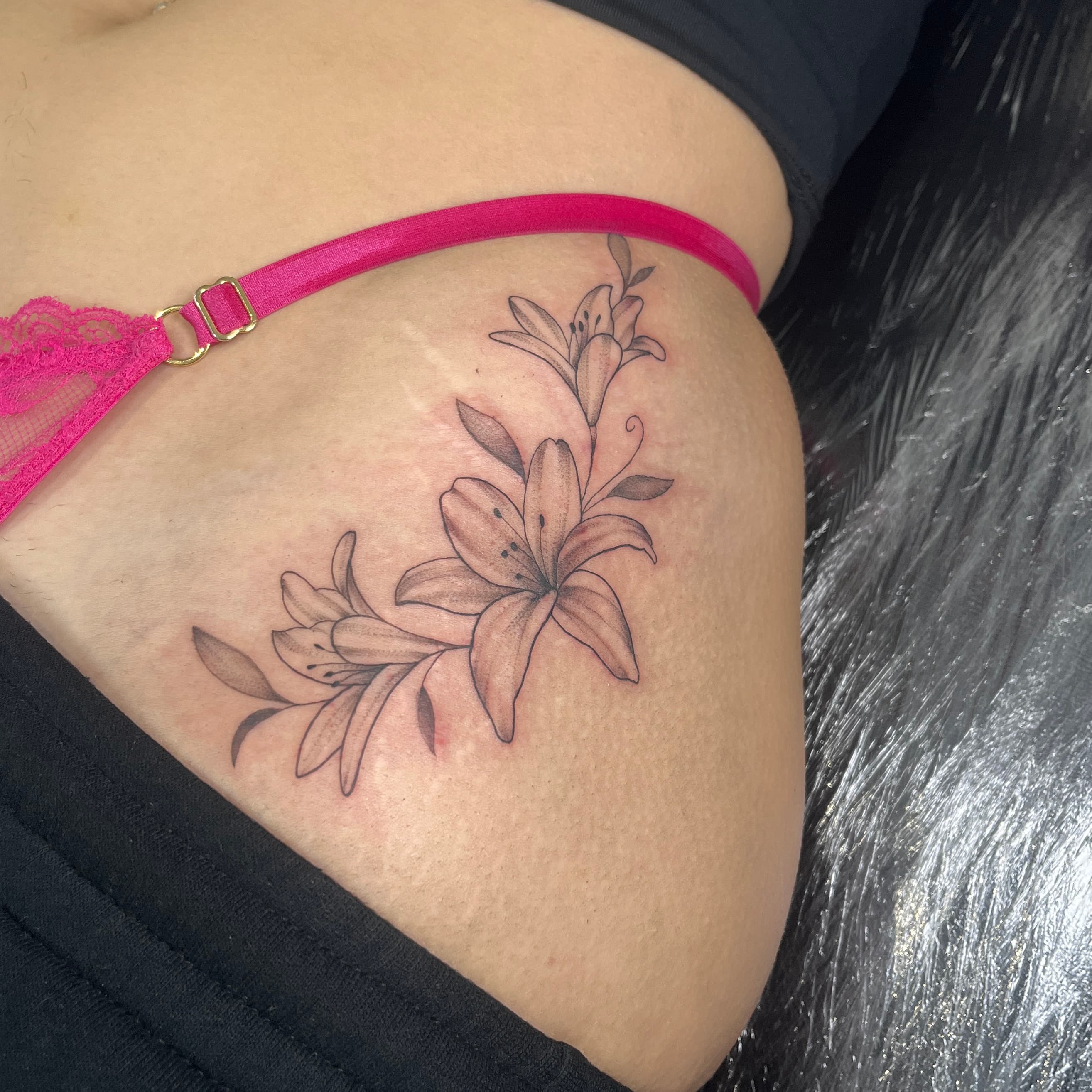 Fine-line floral lillies framing the hip by AinsleyXTattoos